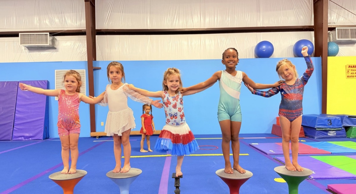 Five girls in the Cheer-nastics class balance on wobble stools with their arms stretched out to each other