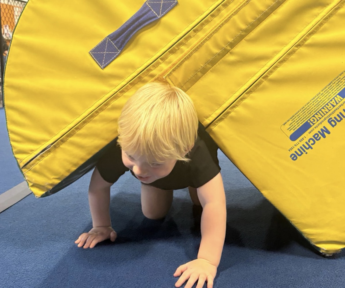 A young ninja crawls under a yellow mat at Leah's Gymnastics & Cheerleading