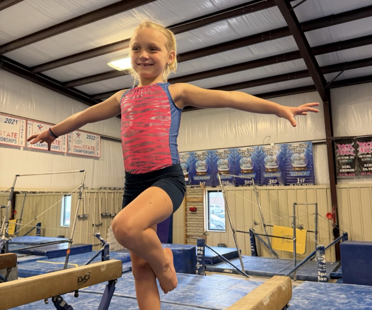 A smiling recreational gymnast balances on one leg on the beam at Leah's Gymnastics & Cheerleading