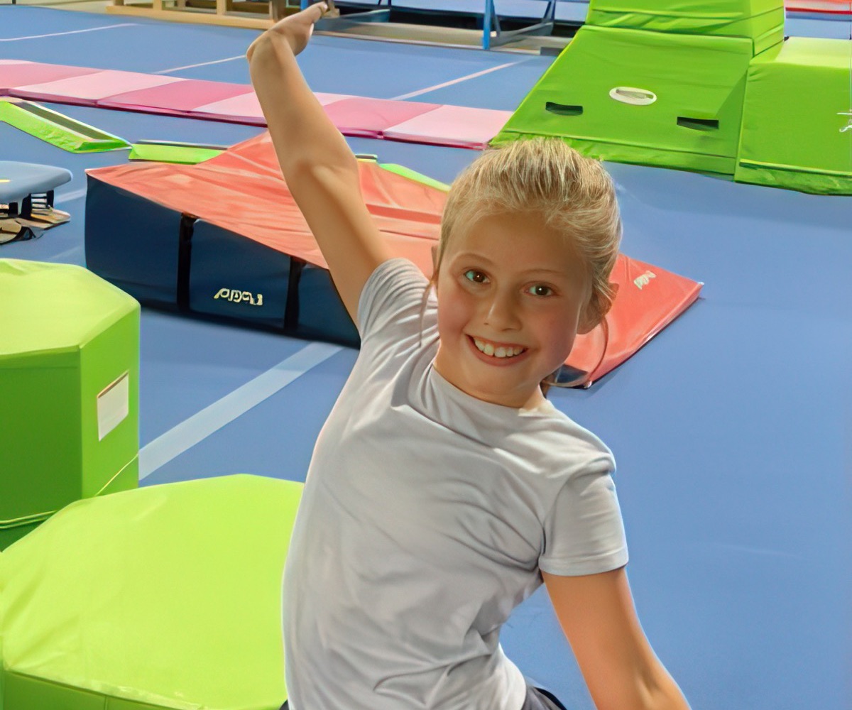 A recreational gymnast strikes a pose with her arm raised in the gym