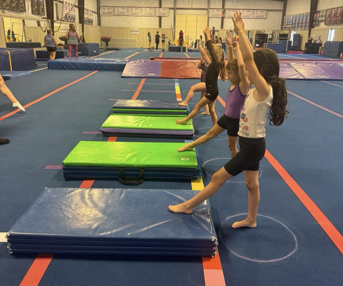 A line of gymnasts reach up and point a toe in a stretching drill