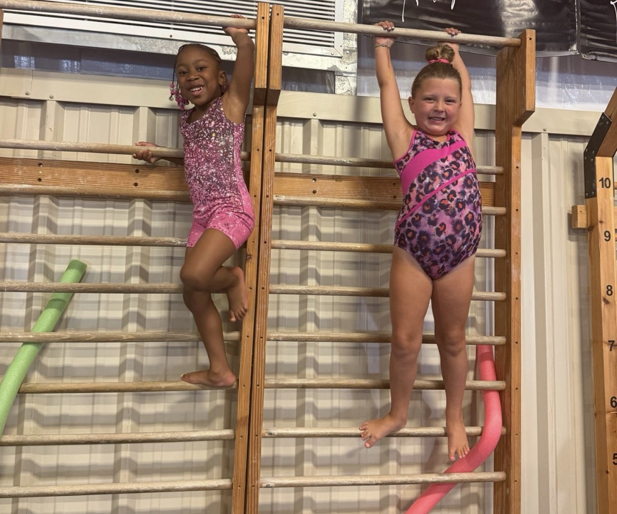 Two gymnasts hang and climb on the wall bars