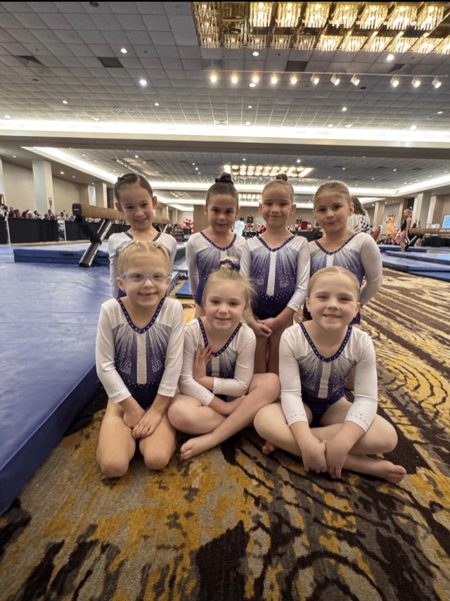 Seven young team gymnasts posing together at a meet