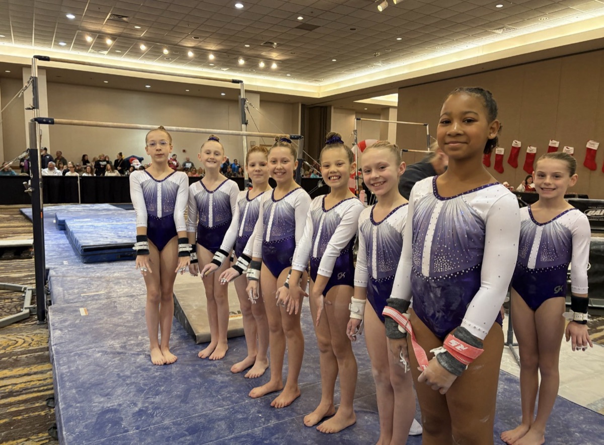 Leah's team gymnasts lined up beside the uneven bars at a meet